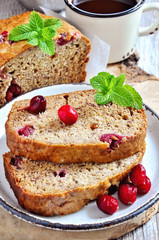 Banana bread loaf with ripe bananas and frozen cranberries on rustic background, selective focus