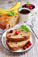 Banana bread loaf with ripe bananas and frozen cranberries on rustic background, selective focus