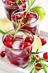 Red refreshing cranberry cocktail with rosemary, lime, and ice cubes, selective focus