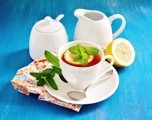 Tea with lemon, mint, and fresh cranberries on  blue background, table setting, selective focus