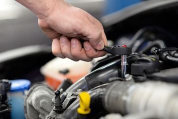Fototapeta na wymiar Mechaniker repariert auto in einer Werkstatt - Detail Hand mit Werkzeug montiert im Motorraum // car repair in garage