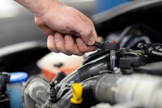 Mechaniker repariert auto in einer Werkstatt - Detail Hand mit Werkzeug montiert im Motorraum // car repair in garage