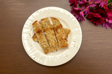 Garlic bread on white plate with flower on wood background