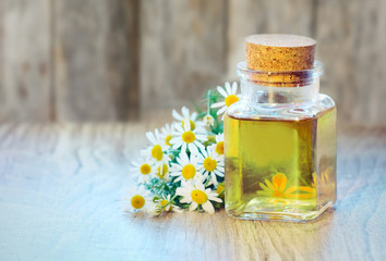 Chamomile oil bottle with flowers on wooden background.