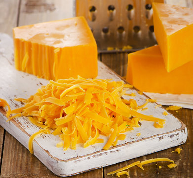 Grated Cheddar Cheese on  wooden Cutting Board.
