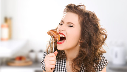 hungry young woman eating meat on fork in kitchen