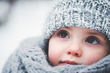 winter close up outdoor portrait of adorable baby girl in grey knitted hat and csarf