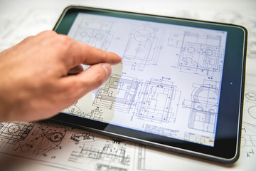 The hand work with tablet (ipod) by blueprints engineering project background - obrazy, fototapety, plakaty