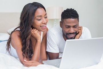 Relaxed couple using laptop on bed