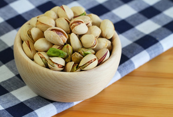 Pistachio nuts in wooden bowl on checkered cloth
