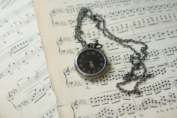 Old watch laying on old piano musical notes