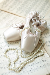Ballet shoes and necklace laying on the old piano musical notes