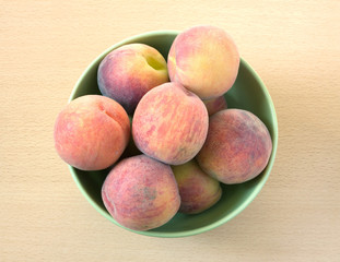Many appetizing peaches in green round bowl on wooden background top view close up