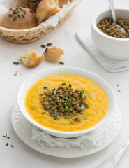 Pumpkin soup with lentils in a white bowl on textiles