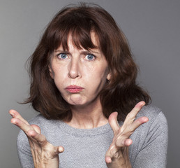 portrait of disappointed 50's woman with both hands opened with tension for exasperation and...