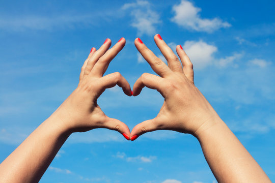 Woman hands forming a heart shape with blue sky