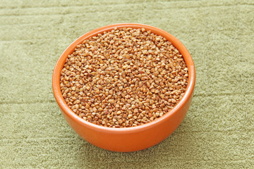 Buckwheat in brown ceramic bowl on taupe fabric taken closeup.