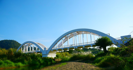 old arch bridge across the creek in LAMPHUN THAILAND. White color arch bridge with blue sky