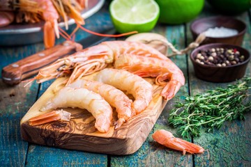 peeled raw shrimps on a wooden cutting board with salt, pepper, lime