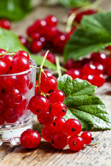 Fresh red currants with leaves in glass on a wooden table, selec