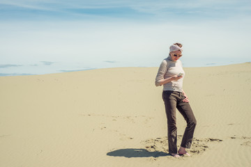 Woman is standing in the desert and is looking at a smartphone