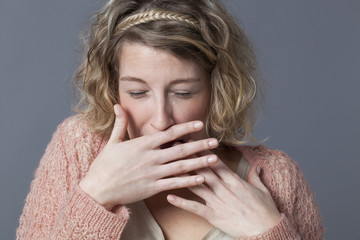 ecstatic young blond woman with curly hair laughing behind her hands for fun and shyness
