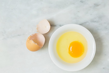 one egg yolk in white bowl and broken egg shells