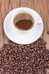 Cup of black coffee and coffee beans on wooden background