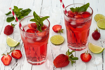 Refreshing summer drink with strawberry, lime and mint in glasses on white wooden background