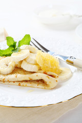 Crepes with honeycomb and bananas on a white plate