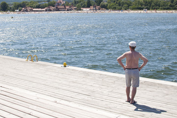 starszy mężczyzna patrzący na plażowiczów z molo