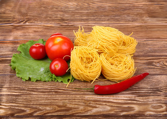 Pasta on the wooden background with tomato, pepper lettuce and pepper