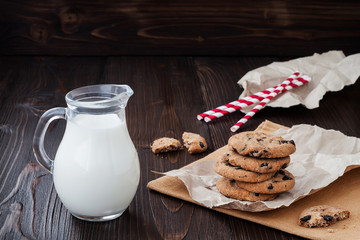 Stack of homemade chocolate chip cookies with milk on dark wooden table