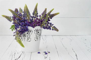 Meadow flowers lupines bouquet in white decorative bucket on vintage white wooden table