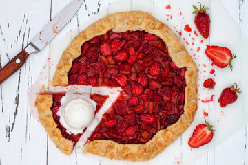 Strawberry and rhubarb galette with ice cream on white vintage wooden background. Top view