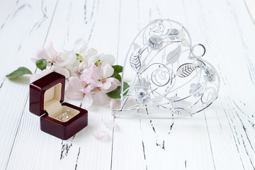 Diamond ring in a box with spring apple tree blossoms and vintage cage heart on white old wooden background. Wedding concept