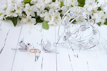 Wedding rings with spring apple tree blossoms and vintage cage heart on white old wooden background. Wedding concept