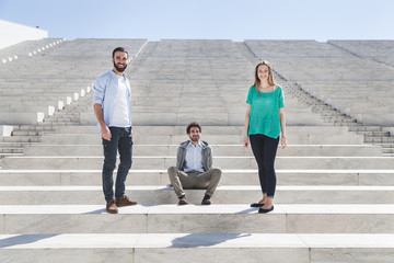 Two men and a girl are sitting on the steps of an outside amphitheater in a summer day