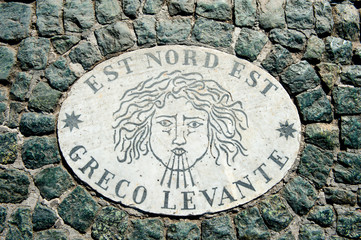 Old wind marker on cobblestone pavement