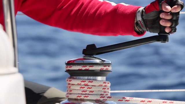 Hands pulling ropes, winding sheets around winches close-up. Sailor's hand on a winch of sailing boat. Sailing.