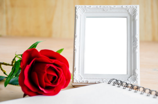 White vintage photo frame and red rose with open diary.