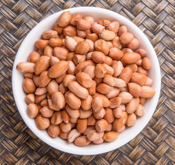 Ground nut or peanuts in white bowl over wicker background