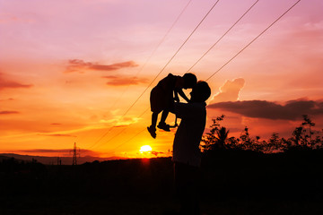 silhouettes of father and son play at mountain range and high voltage electricity pylon sunset background