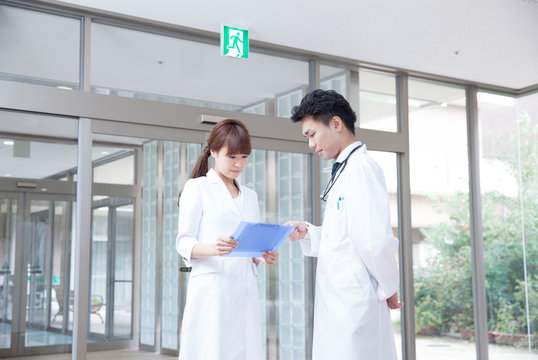 病院内で書類を見ながら話し合う男性医師と女性医師