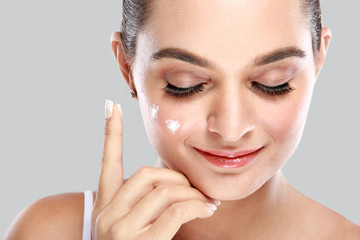 beautiful young woman applying some facial cream on her cheek