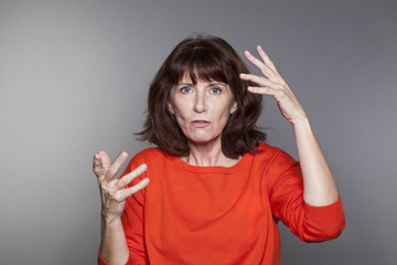 portrait of beautiful 50's woman wearing orange sweater explaining something with both hands up