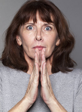 closeup portrait of anxious 50's woman holding breath, praying for success with both hands together in front of chin