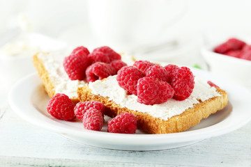 Fresh toast with cream cheese and raspberries on white wooden ba