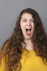 stressed out overweight 20's woman with long brown hair screaming loud for expressing rage and anger
