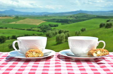 Coffee and cantuccini on the table against Tuscan landscape. Ita